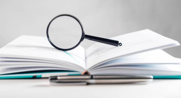 Magnifying lens over open paper book with pages. Concept of academic research. Magnifying lens over open paper book with pages. Concept of academic research.